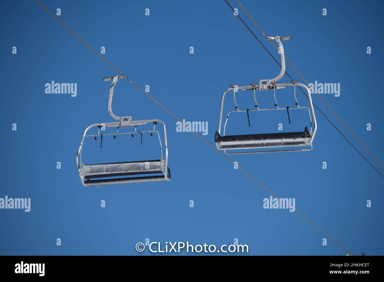 two empty silver metal ski or snowboard chairlift chairs at ski resort  clear blue sky background chairs hanging from cable wire high above horizontal Stock Photo