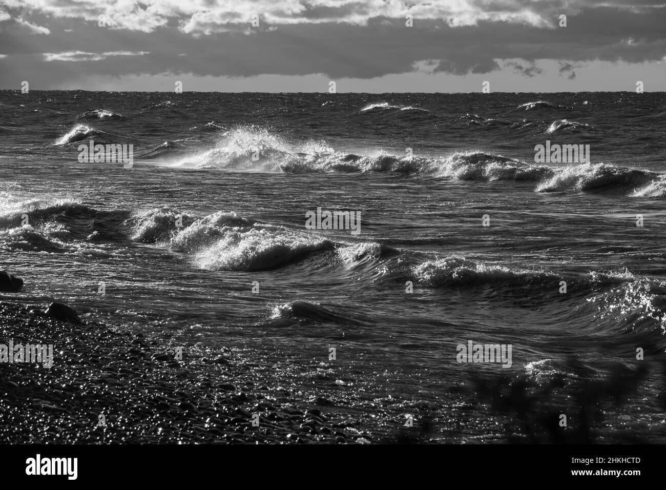 black and white images of waves crashing onto beachfront of fresh water Lake Ontario in Ontario Canada on fall day horizon and clouds in background Stock Photo