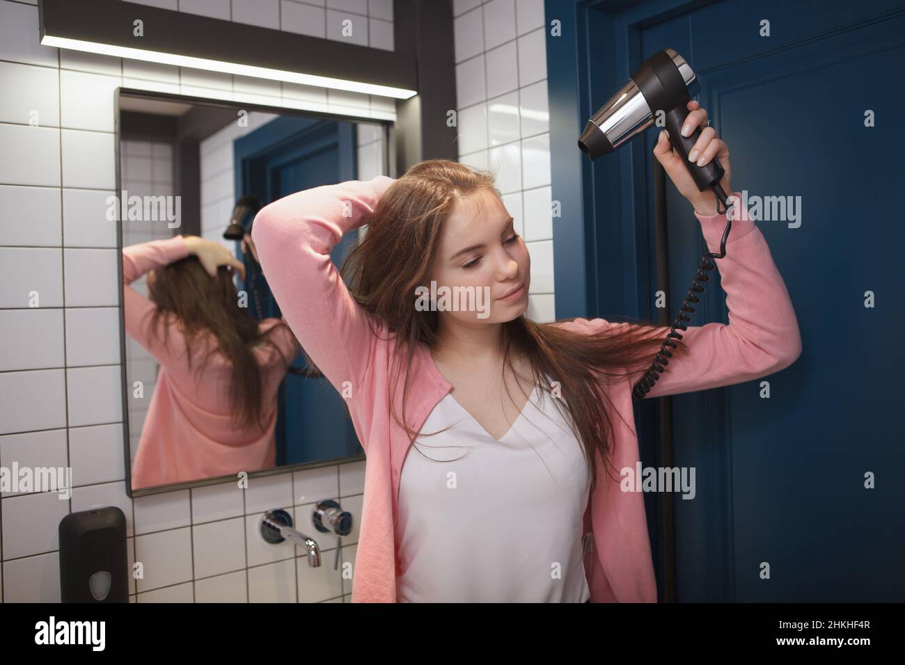 Charming young woman blow drying her hair in the bathroom Stock Photo ...