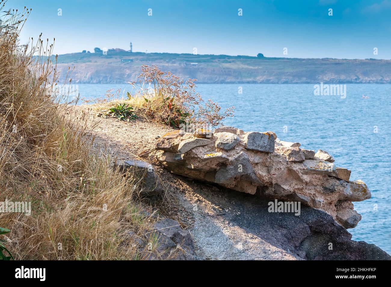 Mountain ledge and path with a fragment of rock and grass against the blue sky and the sea Stock Photo