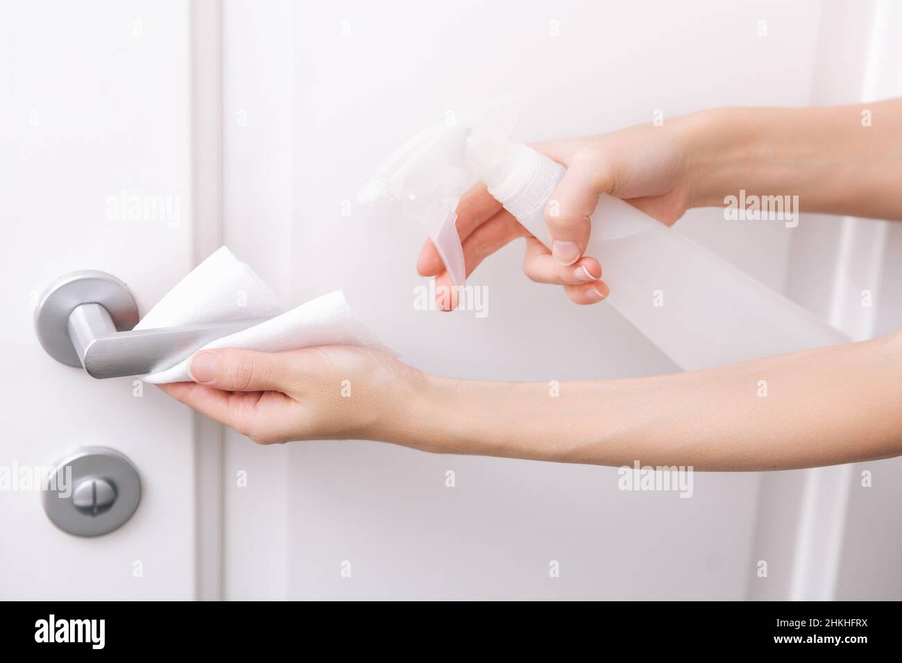 Cleaning white door handles with an antiseptic wet wipe and sanitizer spray. Disinfection in hospital and public spaces against corona virus. Woman Stock Photo