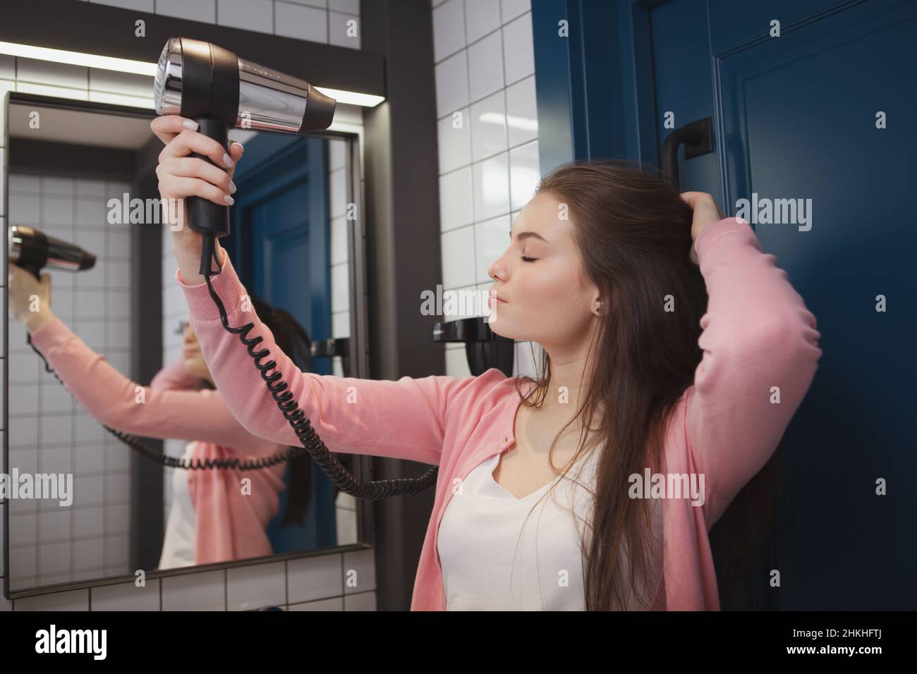 Gorgeous young woman blow drying her hair in hostel bathroom Stock ...