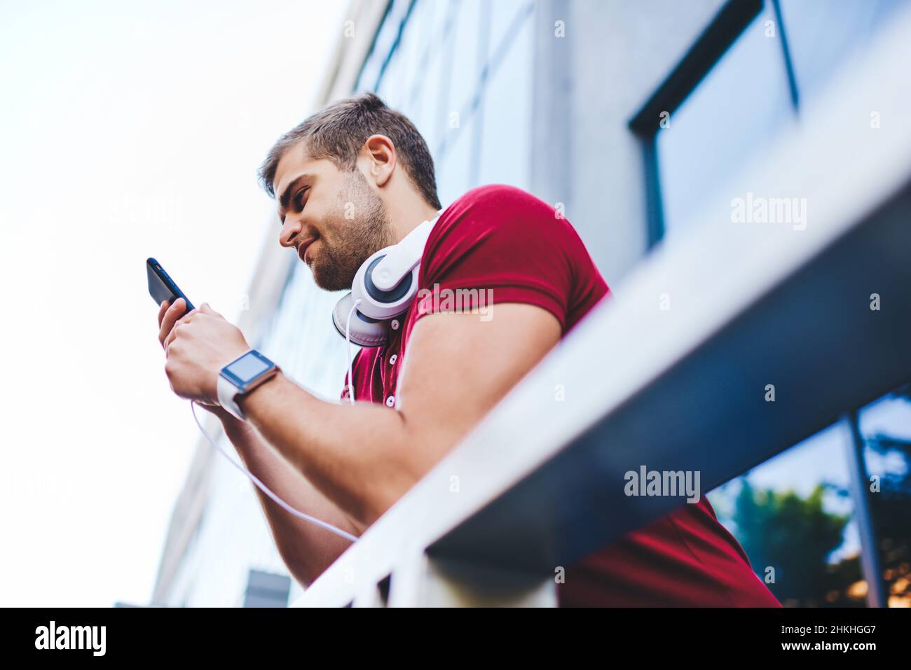 Positive young guy messaging via smartphone while leaning on railing Stock Photo