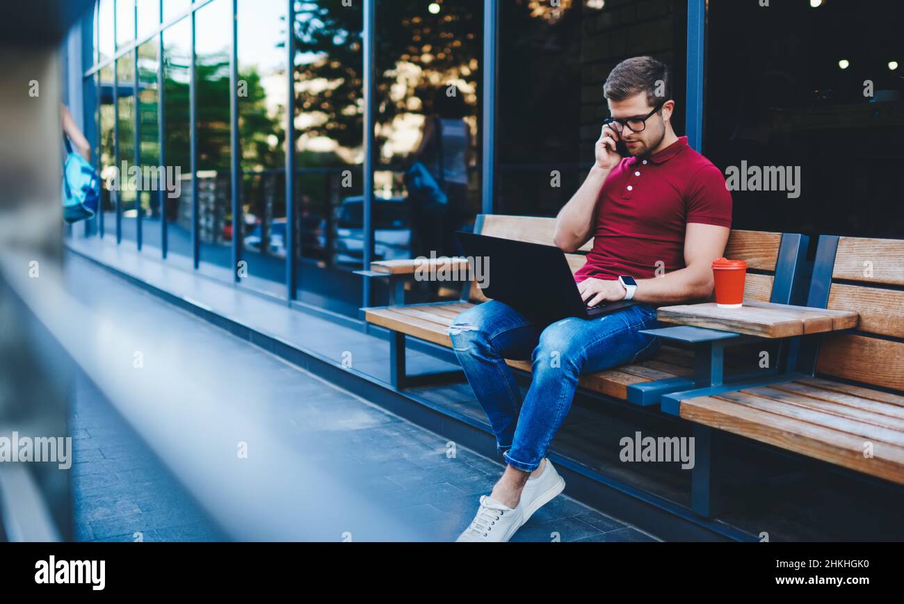 Serious male freelancer using laptop while talking on phone Stock Photo
