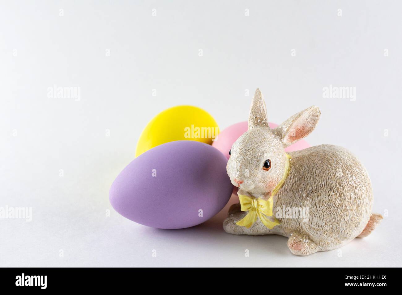 Easter bunny figurine with three Easter eggs on white background with copy space. Stock Photo