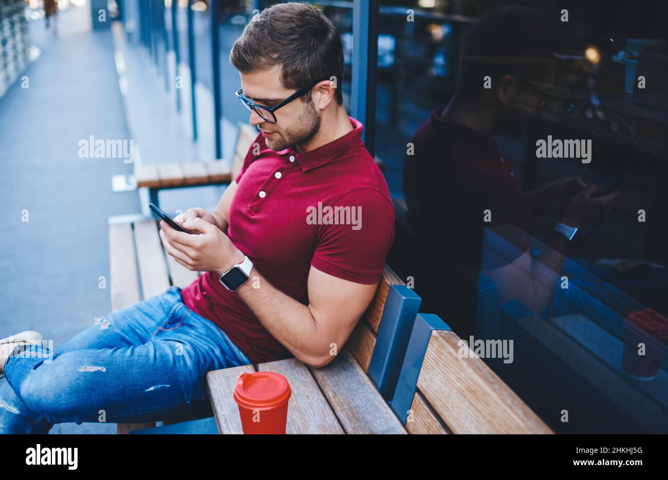 Serious young guy resting on bench while surfing cellphone Stock Photo