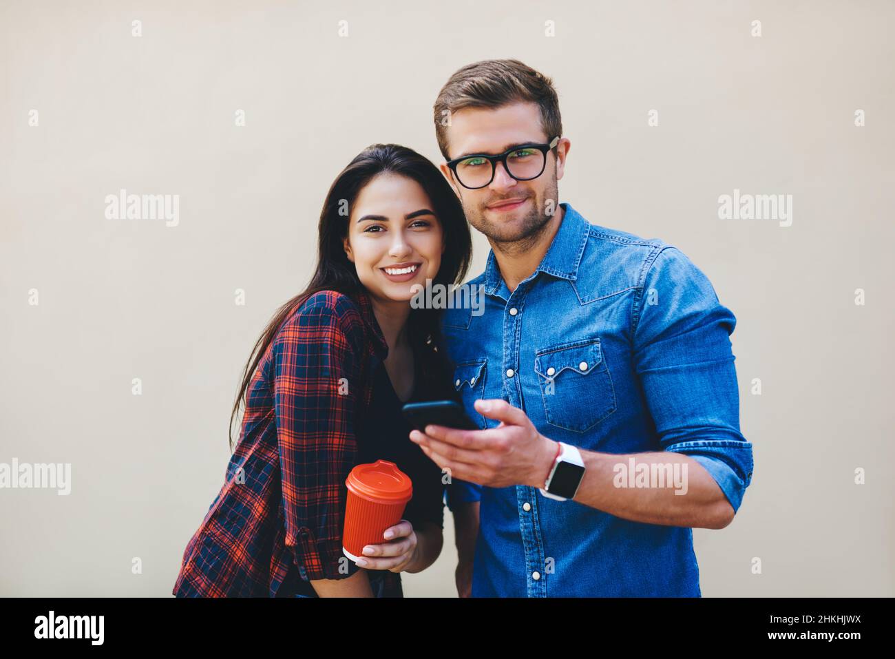 Happy couple with takeaway coffee and smartphone against beige wall Stock Photo