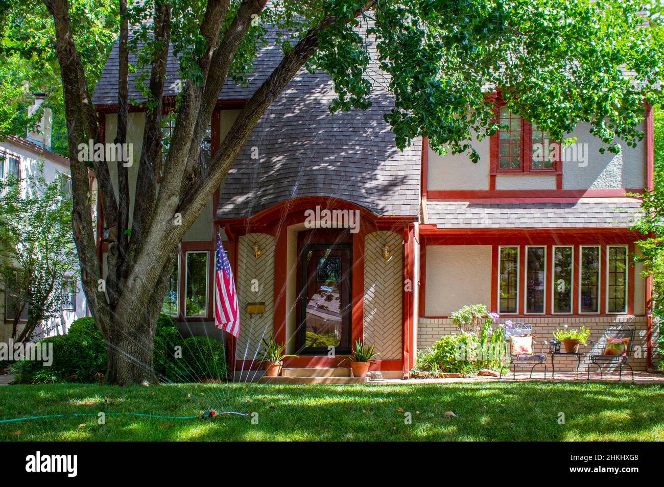 Pretty brick house trimmed in red with patio and flowers and big trees ...