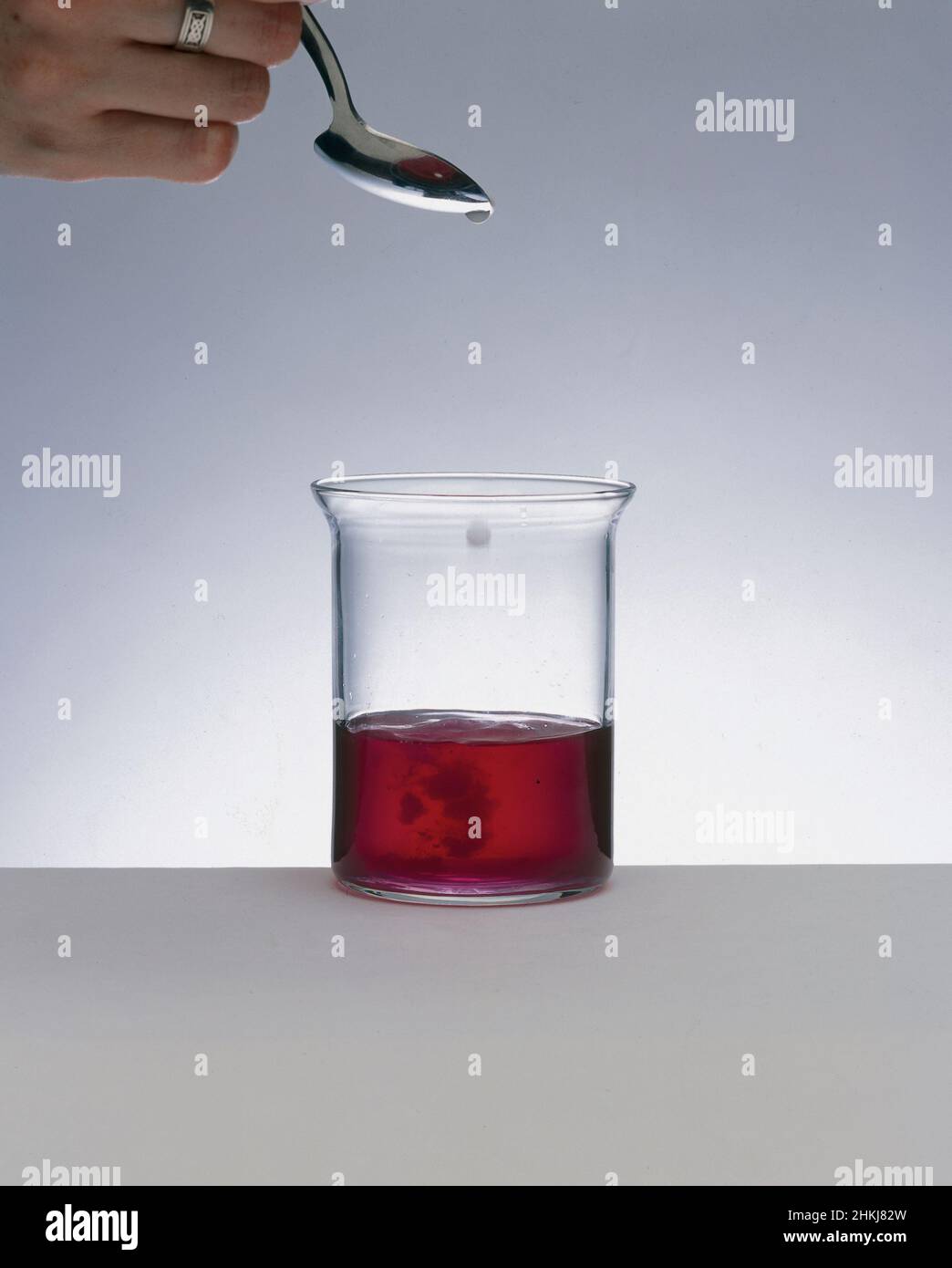 Clear liquid dripping into a beaker containing red liquid Stock Photo