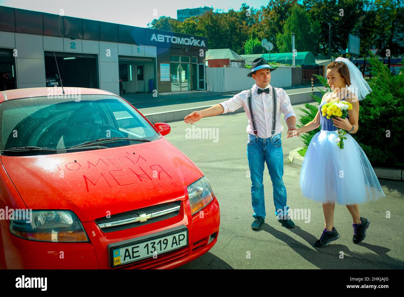 Dnepropetrovsk, Ukraine - 09.11.2016: A young man in a hat and a woman with a bouquet of flowers near the car. On the hood in Russian is written 'wash Stock Photo