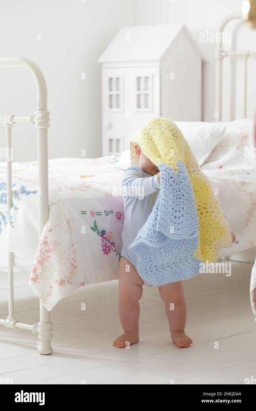 Baby boy standing next to bed with blanket over his head Stock Photo
