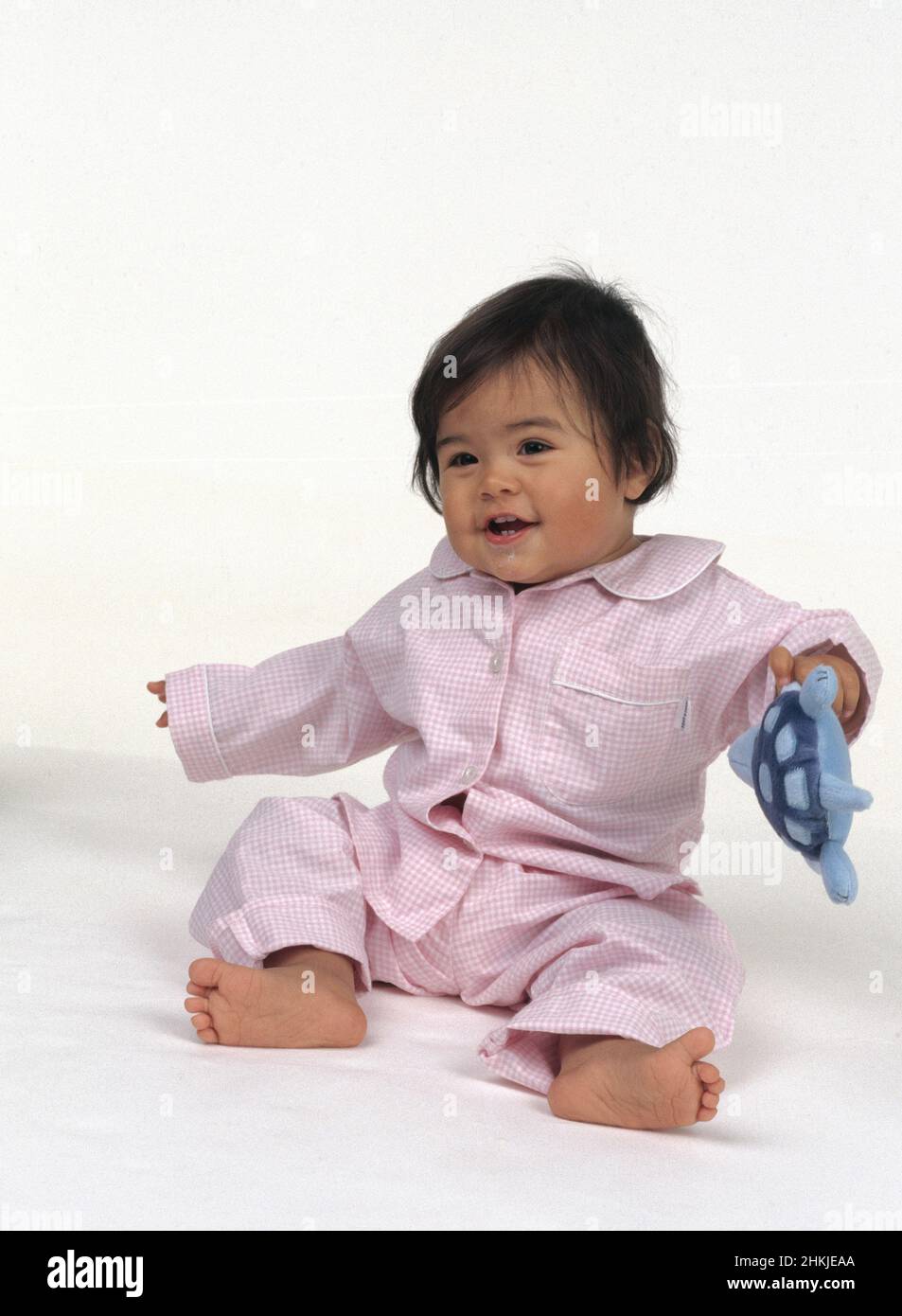 Baby sat on the floor wearing pink check pyjamas Stock Photo