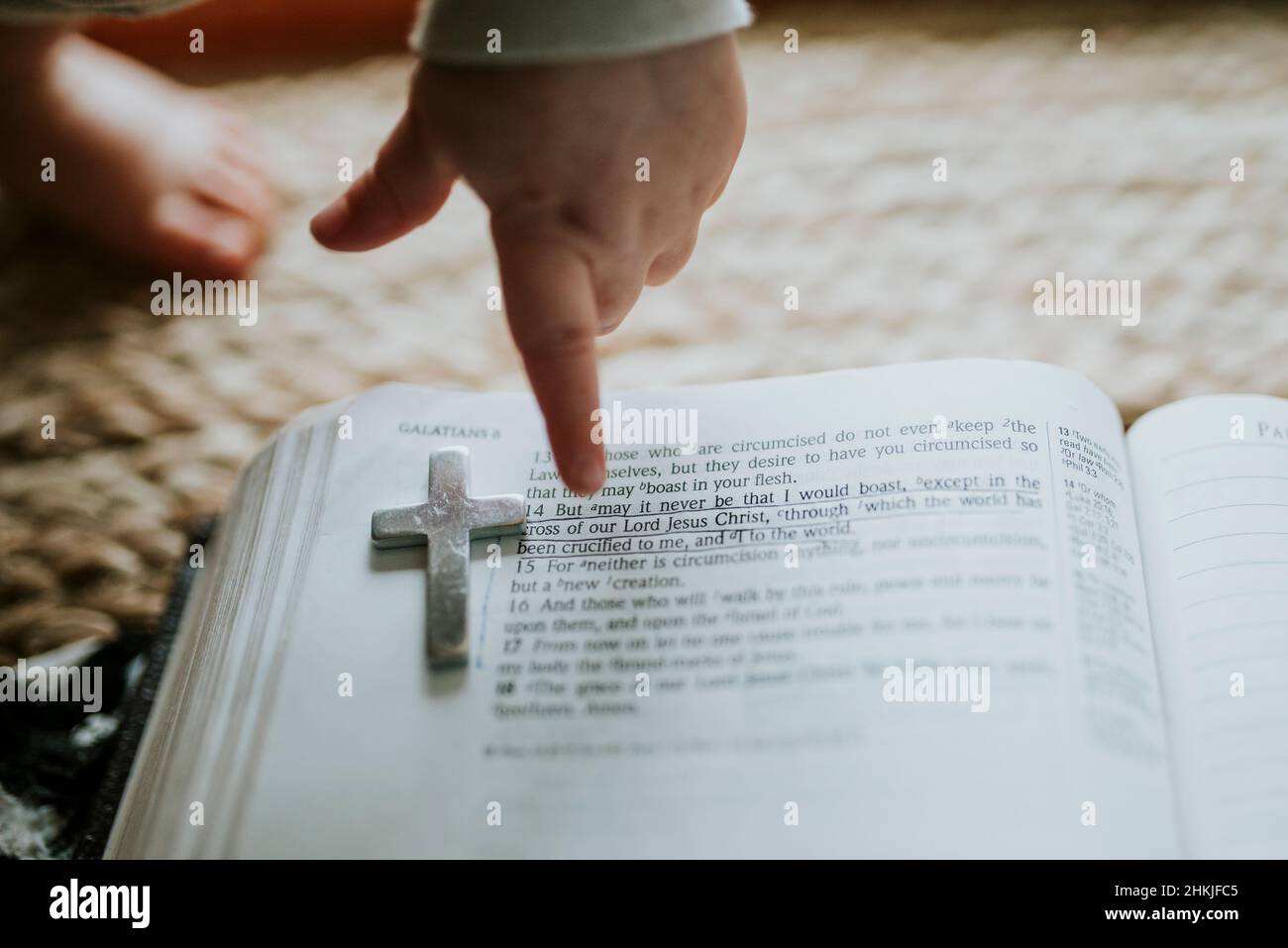 Child's hand pointing to Bible verse with metal cross on page Stock Photo