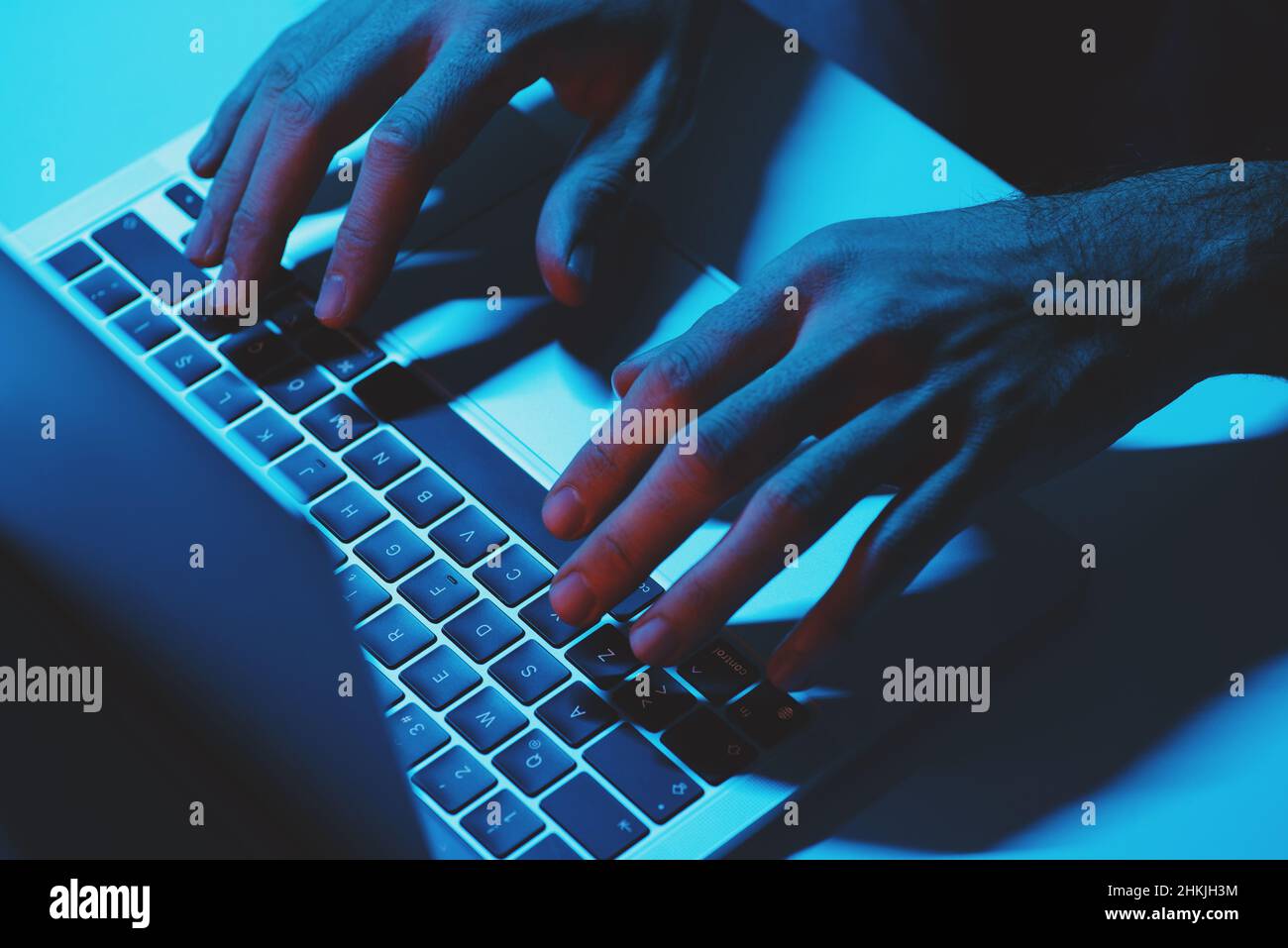 A man Using a laptop computer under blue light. Stock Photo
