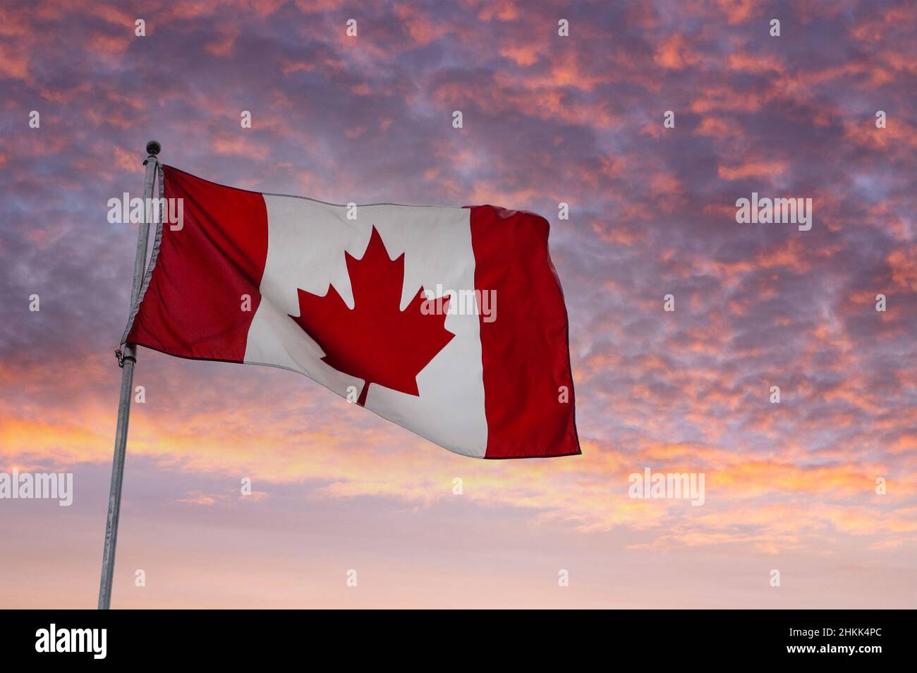 Flag of Canada flying on a pole against a sunrise background. Stock Photo