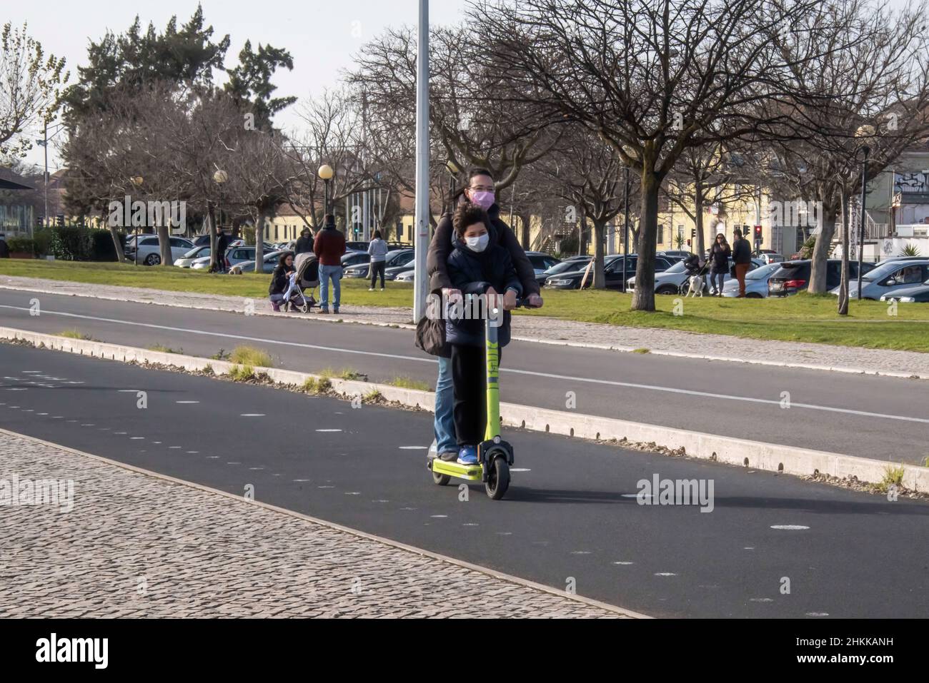 People wearing protective masks ride a scooter on the boulevard near the 25 de Abril Bridge. The Portuguese Council of Ministers has approved a Law Decree that puts an end to the requirement, for those entering Portugal, 'to present a test with a negative result to those who present the EU covid-19 digital certificate in any of its modalities or another vaccination test that has been recognized'. Stock Photo