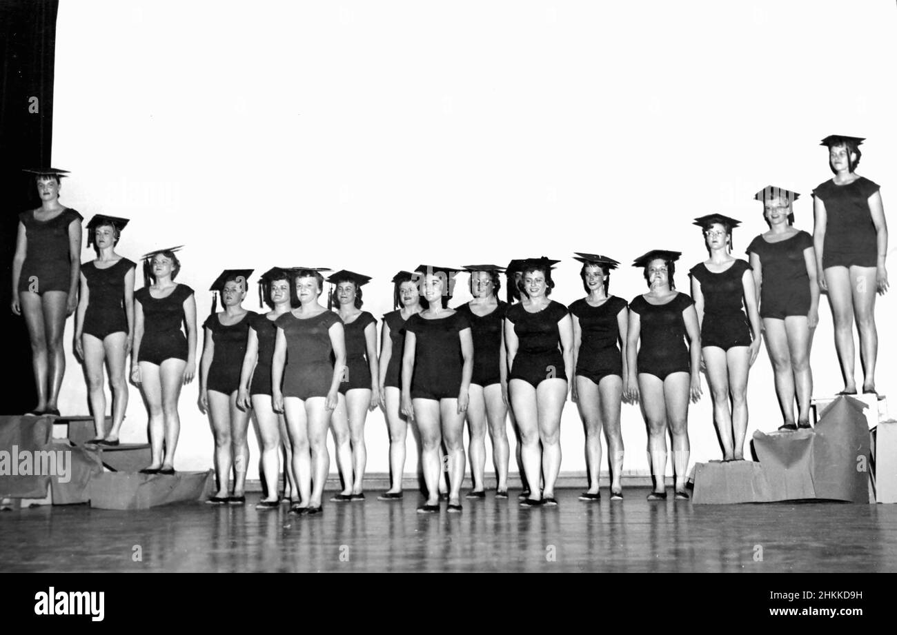 A line up of young women wearing leotards wear their graduation  mortarboards, ca. 1955. Stock Photo