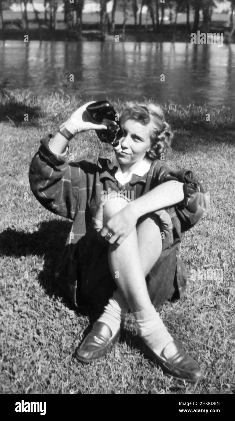 A young woman pretends to empty a flask of liquor on a picnic, ca. 1940. Stock Photo