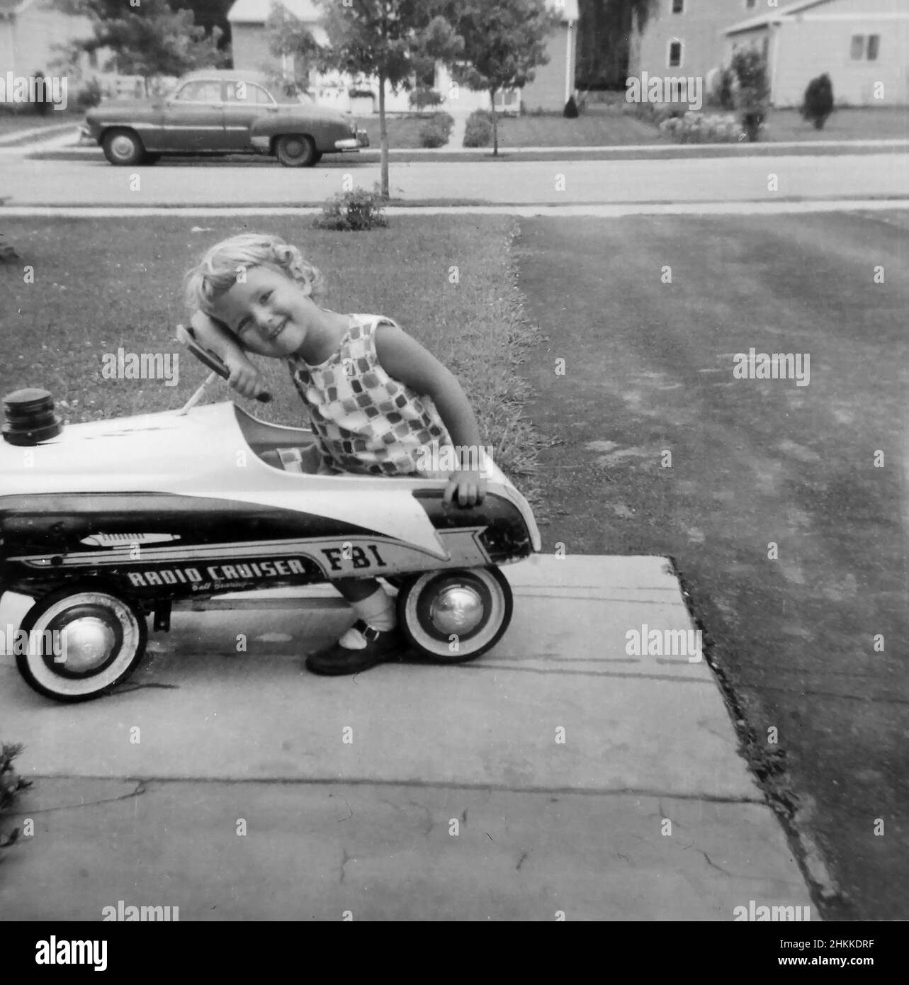A young girl pauses while playing her toy car, ca. 1950. Stock Photo