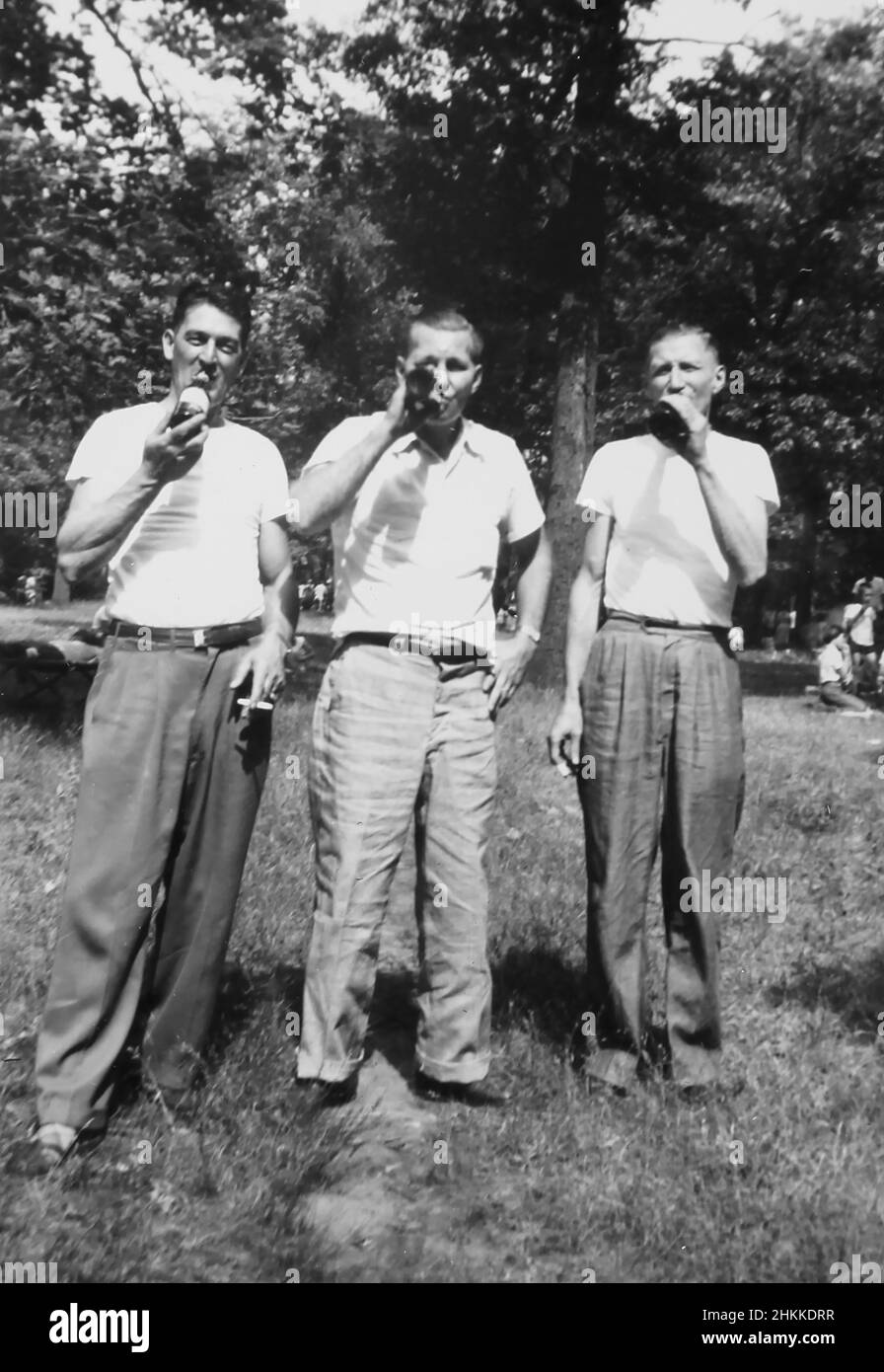 Three men drink from beer bottles, ca. 1950. Stock Photo