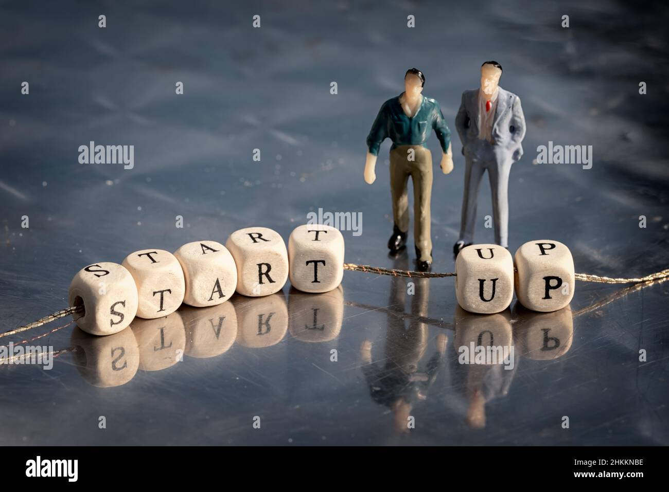 Miniature model of businessmen and wooden cubes with start up inscription strung on a thread on reflective table. Stock Photo