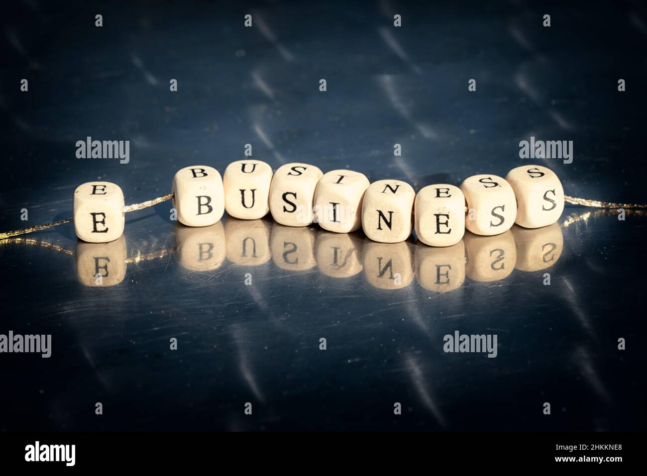 Wooden cubes with e business inscription strung on a thread on reflective table. The online business concept. Stock Photo