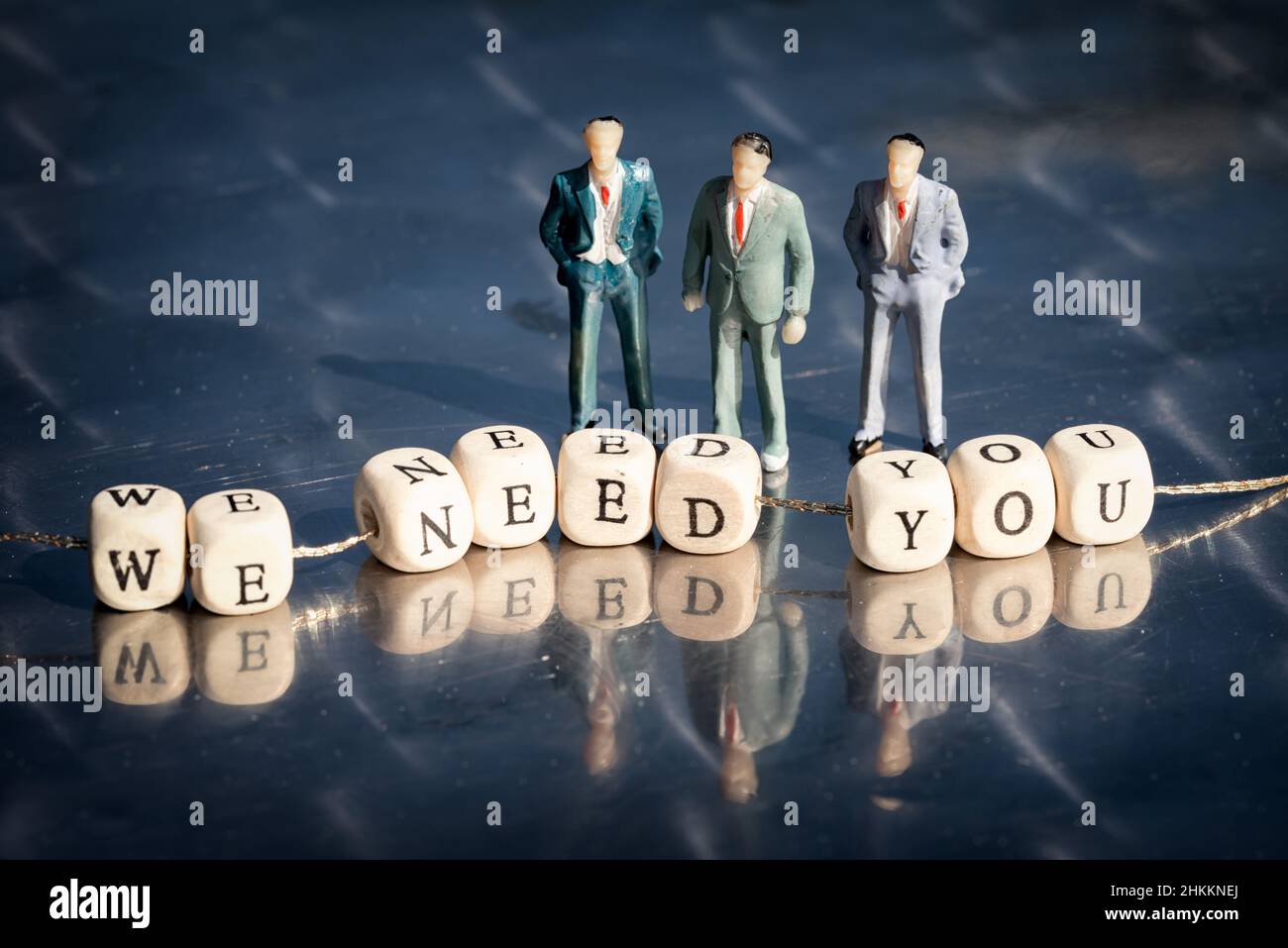 Miniature model of businessmen and wooden cubes with we need you inscription strung on a thread on reflective table. The recruitment business concept. Stock Photo