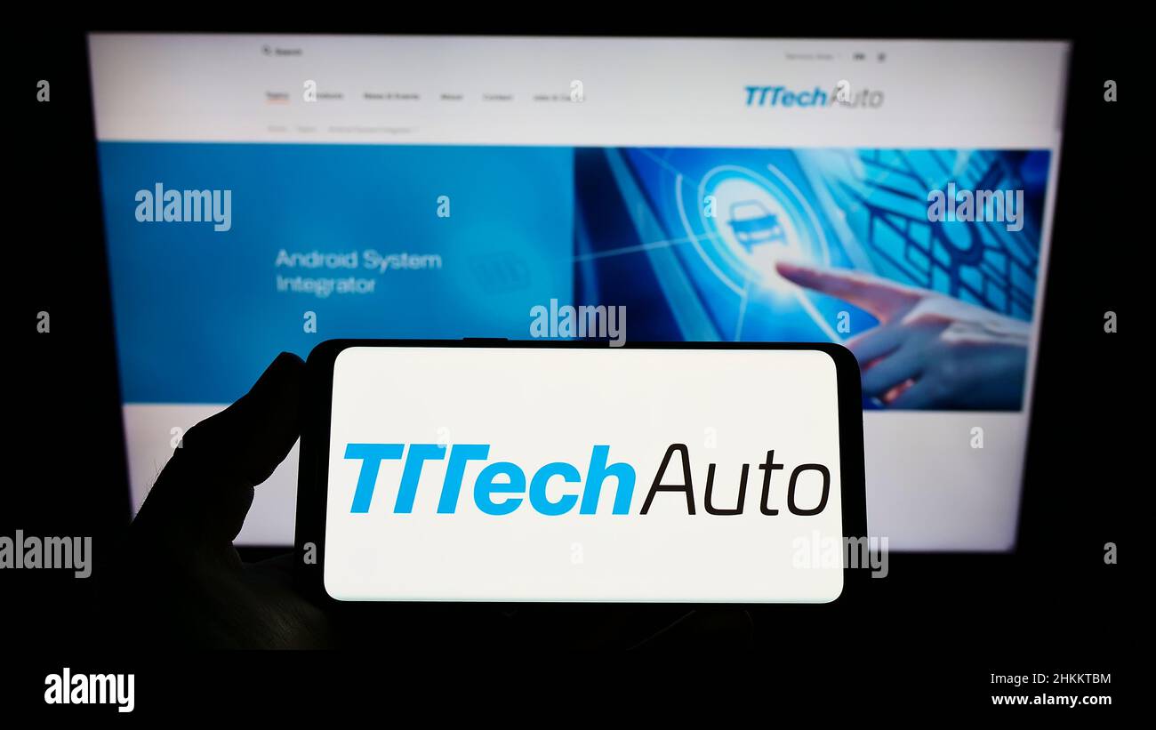 Person holding smartphone with logo of autonomous driving company TTTech Auto AG on screen in front of website. Focus on phone display. Stock Photo