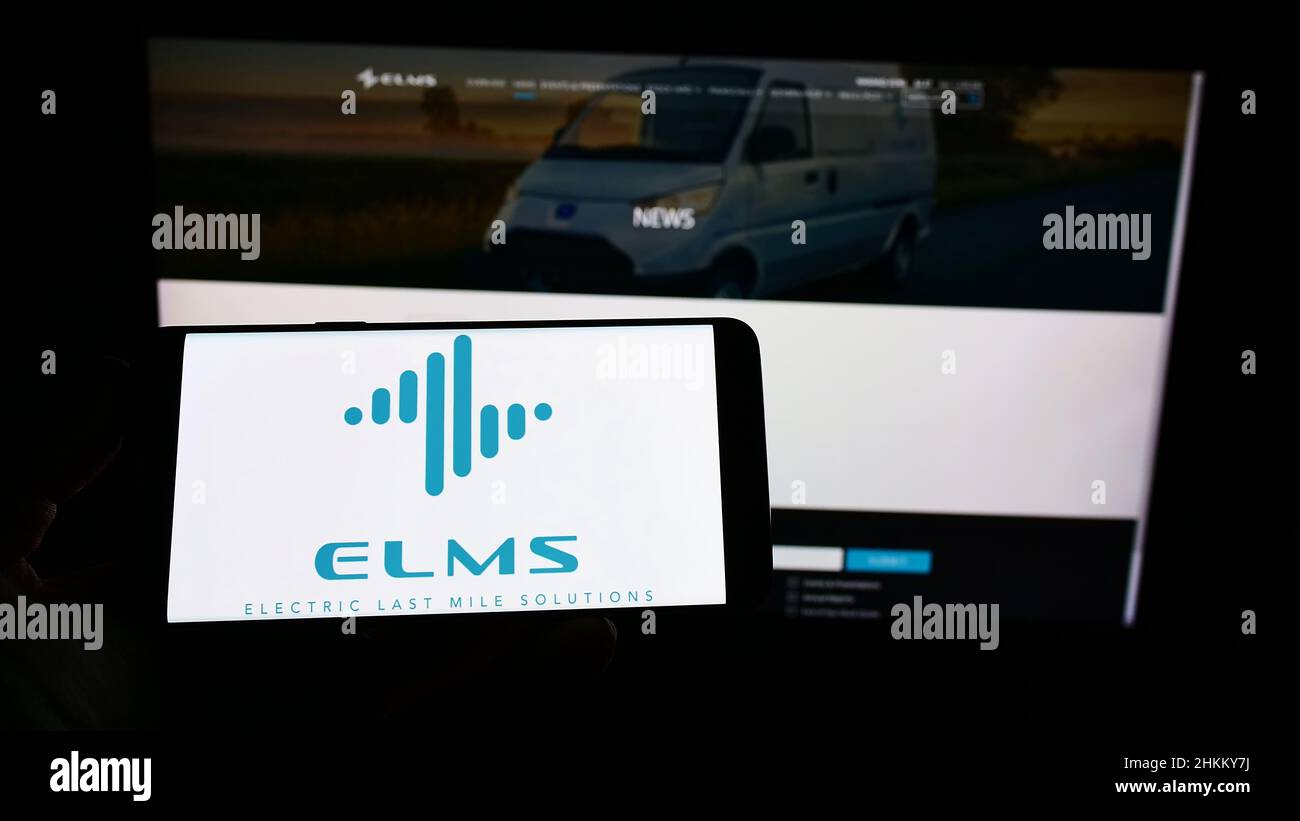 Person holding smartphone with logo of US company Electric Last Mile Solutions Inc. (ELMS) on screen in front of website. Focus on phone display. Stock Photo