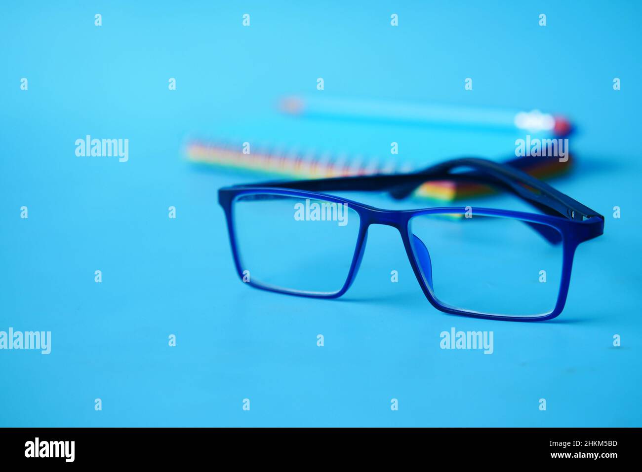 notepad, eyeglass and a pencil on blue background  Stock Photo