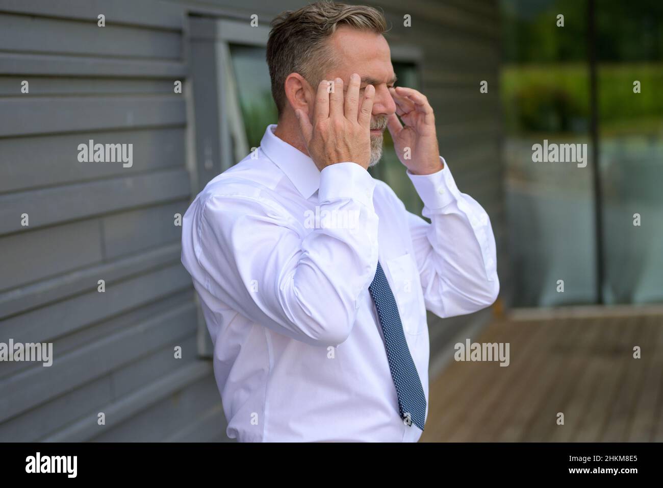Distressed or anxious senior man raising his hands to the sides of his head as he stands on an undercover urban walkway Stock Photo