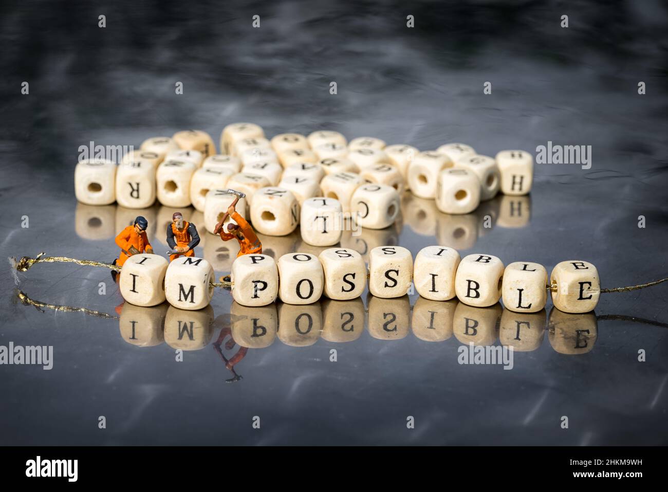 Miniature model of people remove wooden cubes with word impossible to