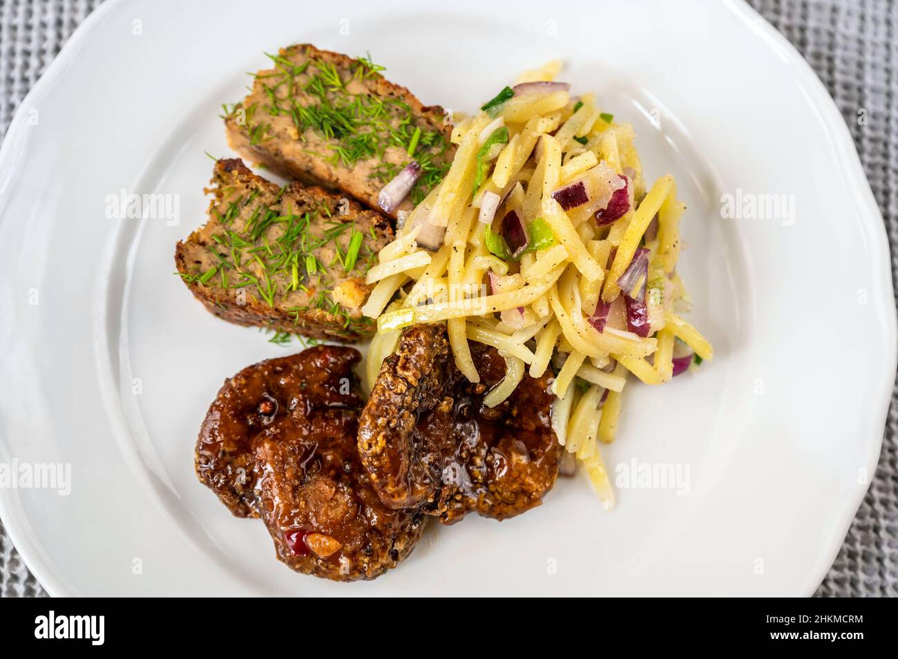 Soy meat steak with sauce, vegetable stuffing, potato salad cut into thin noodle (julienne) with onion on white plate, closeup. Stock Photo