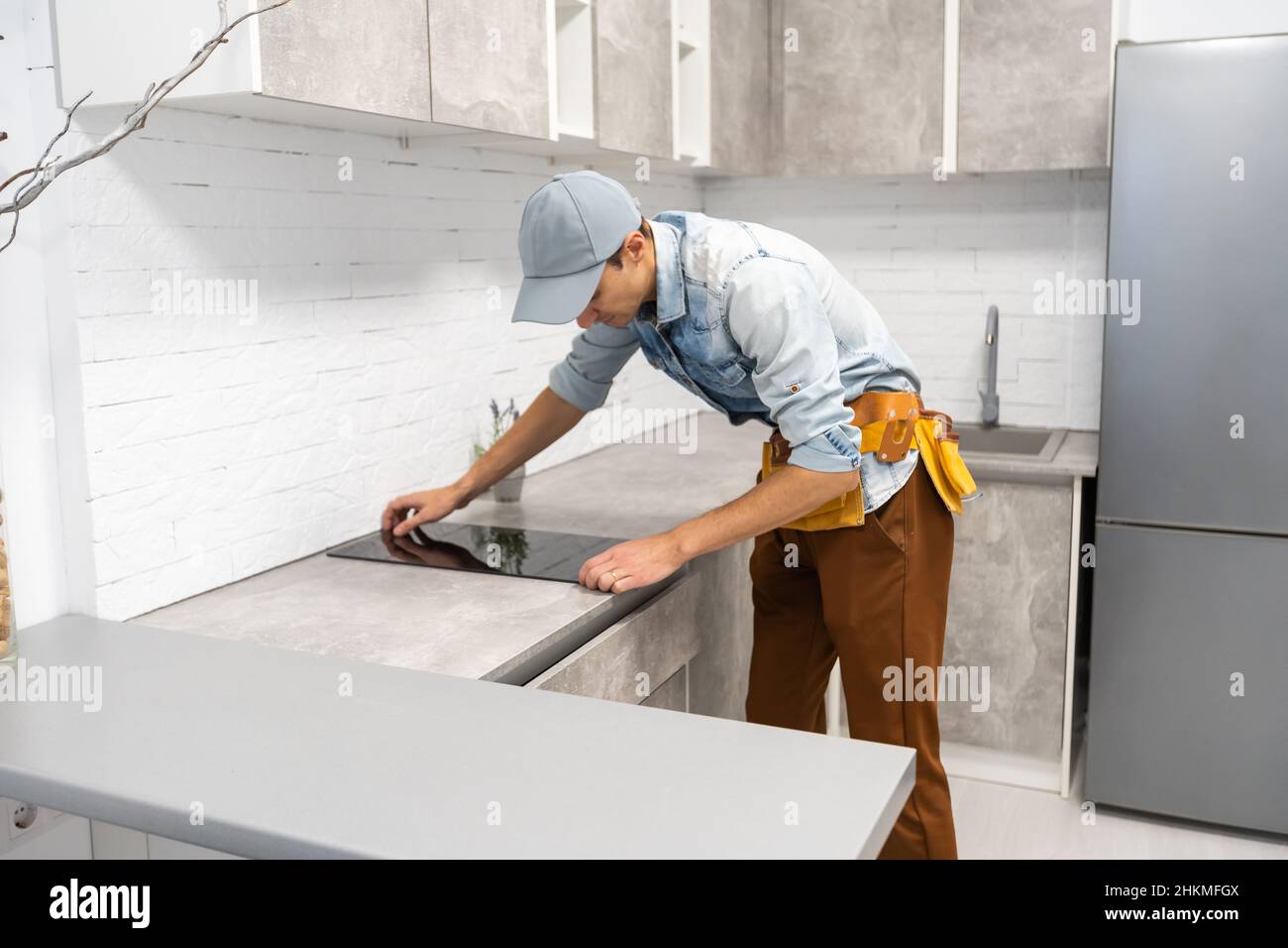Master installs electric hob on kitchen cabinet. Stock Photo