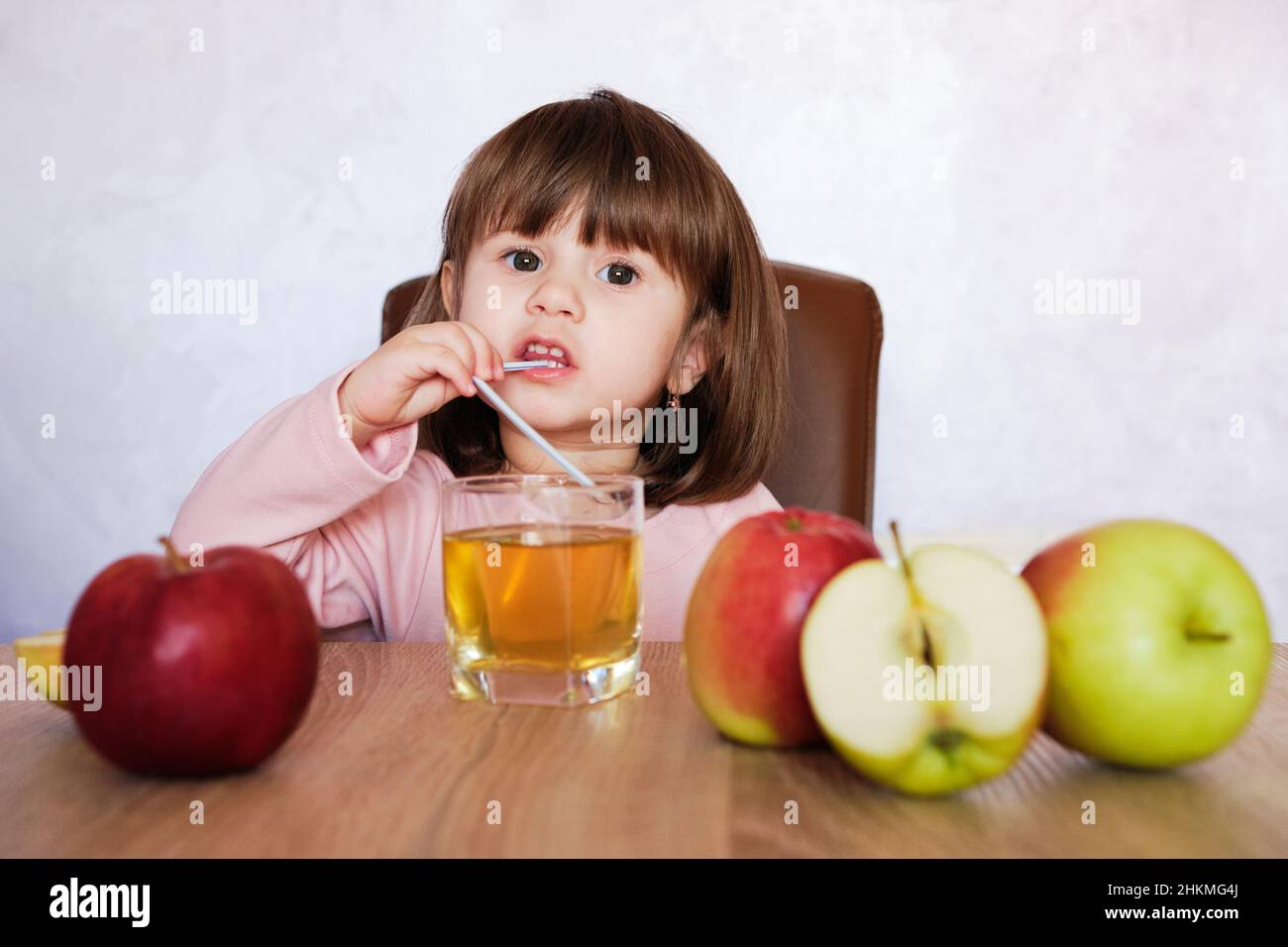 Cute little girl drinks apple juice using drinking straw. Baby girl with juice and fruit apples. Healthy food. Stock Photo
