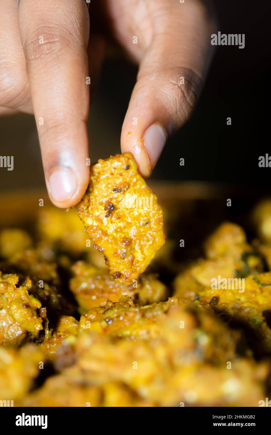 Human hand picking cooked and spicy chicken piece for eating. Stock Photo