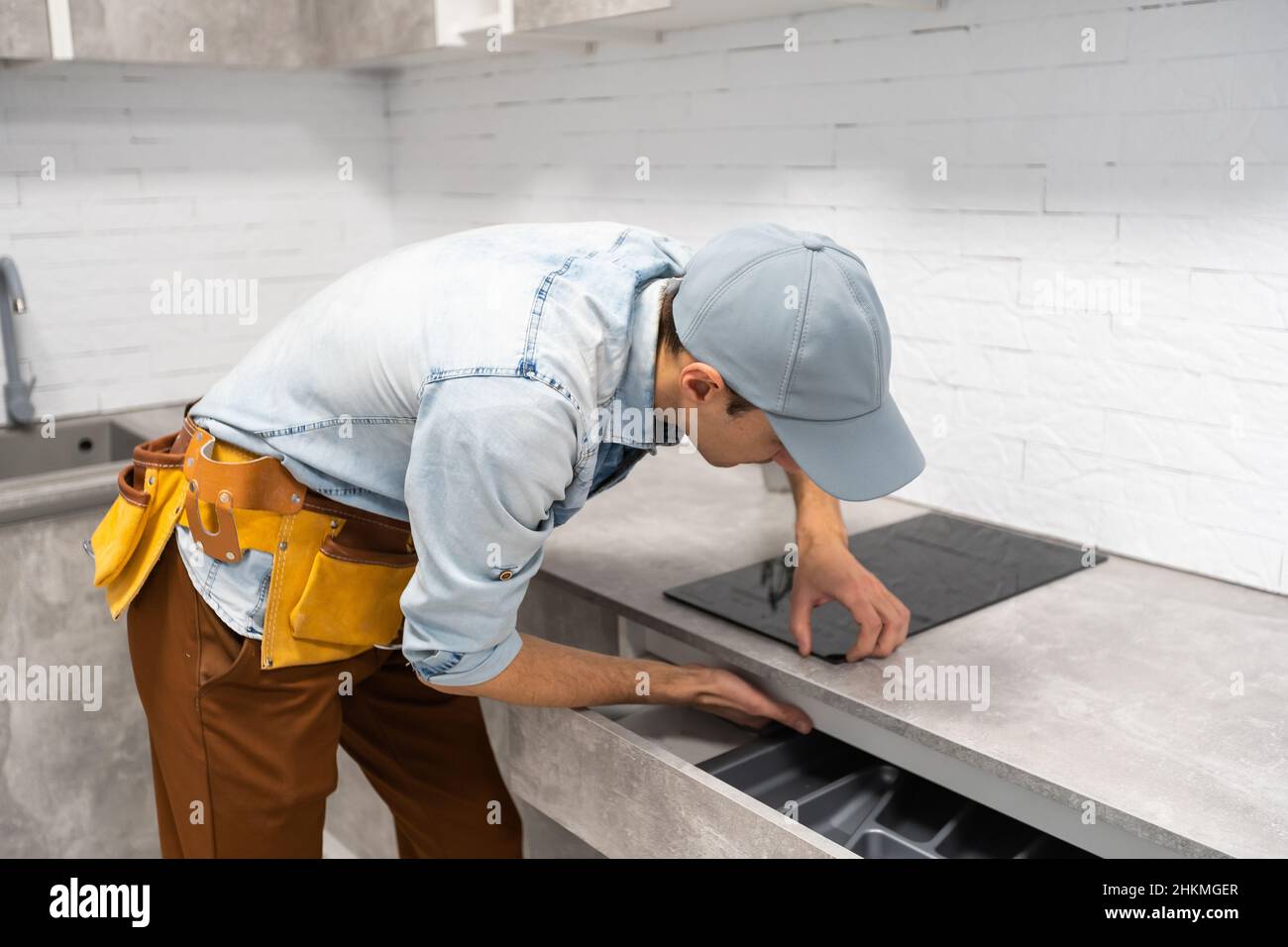 Master installs electric hob on kitchen cabinet. Stock Photo