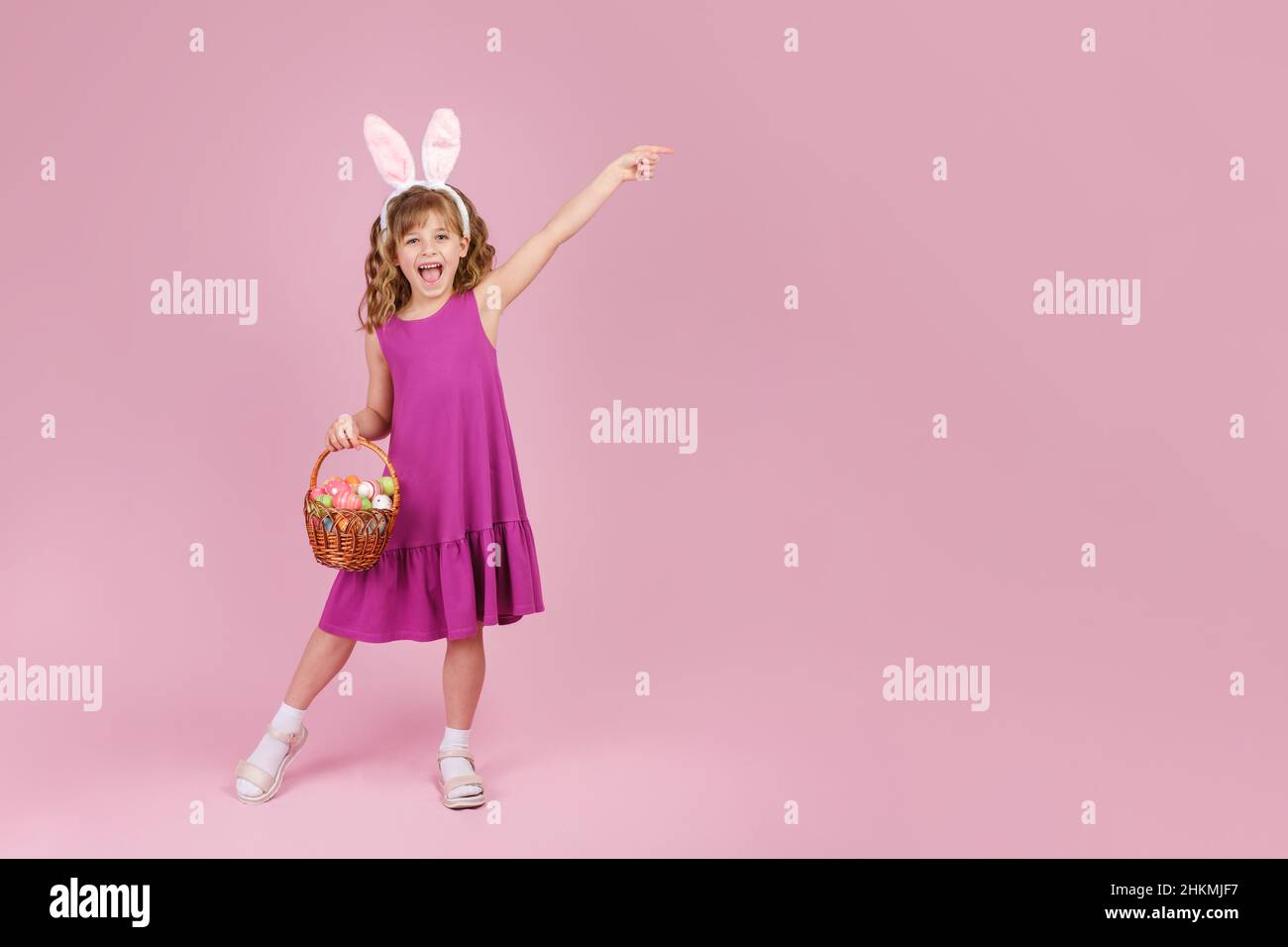 Girl in Easter bunny ears holds in hands a basket with eggs on pink background Stock Photo