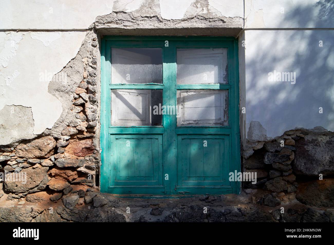 green painted wooden windows with internal shutters typical construction canarian house with render broken to reveal volcanic rock construction Teguis Stock Photo