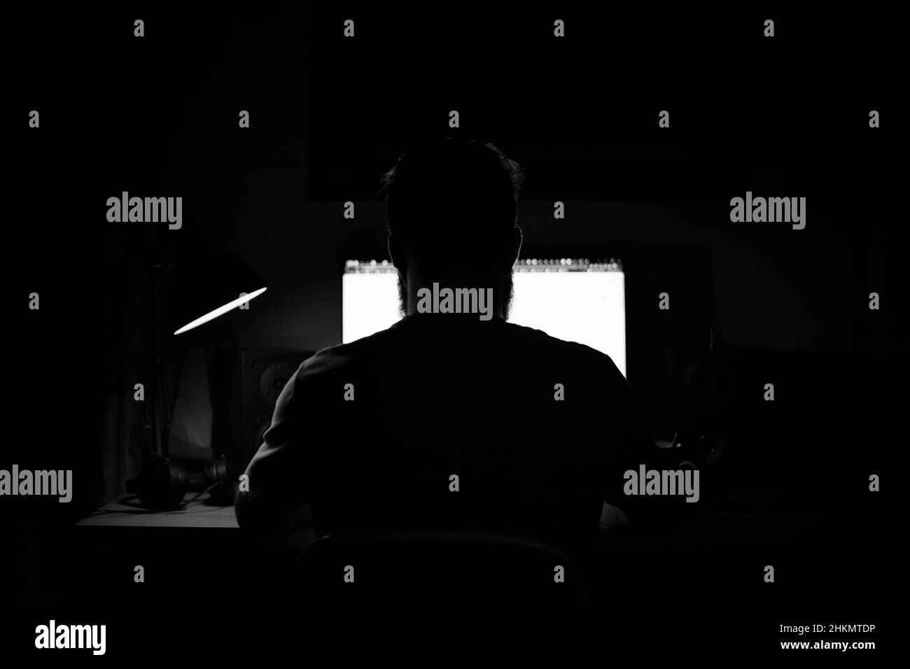 A man sits at a computer in a room at a table at nigh programming black and white Stock Photo