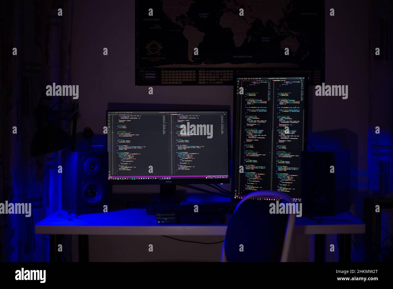 A man sits at a computer in a room at a table at night with blue lighting and programs Stock Photo