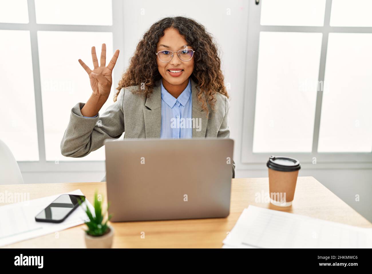 Beautiful hispanic business woman sitting on desk at office working ...