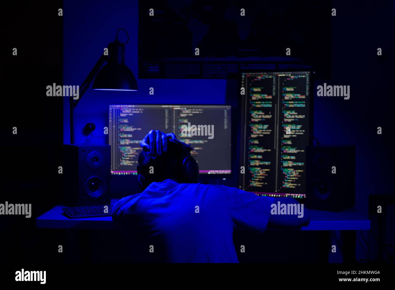 A man sleep at a computer in a room at a table at night with blue lighting and programs Stock Photo