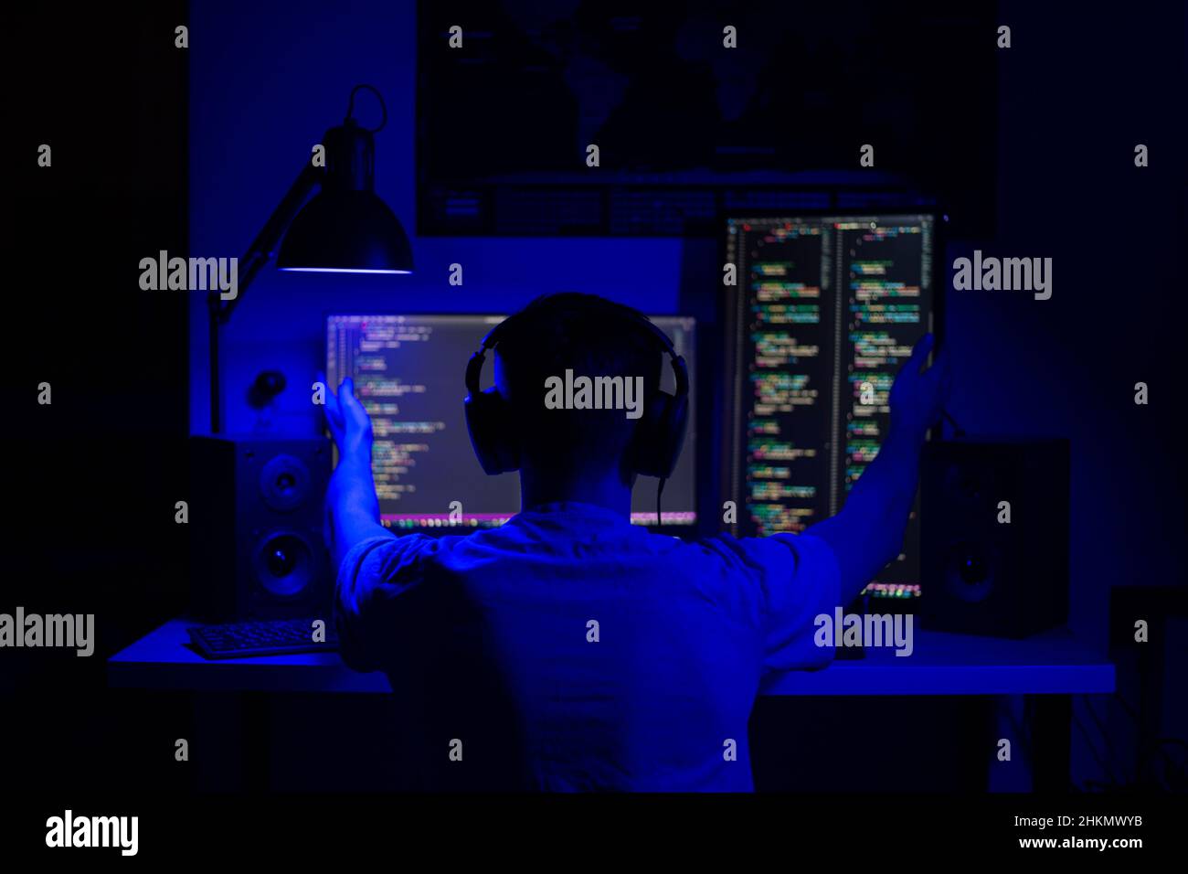 A disappointed man sits at a computer in a room at a table at night with blue lighting and programs Stock Photo