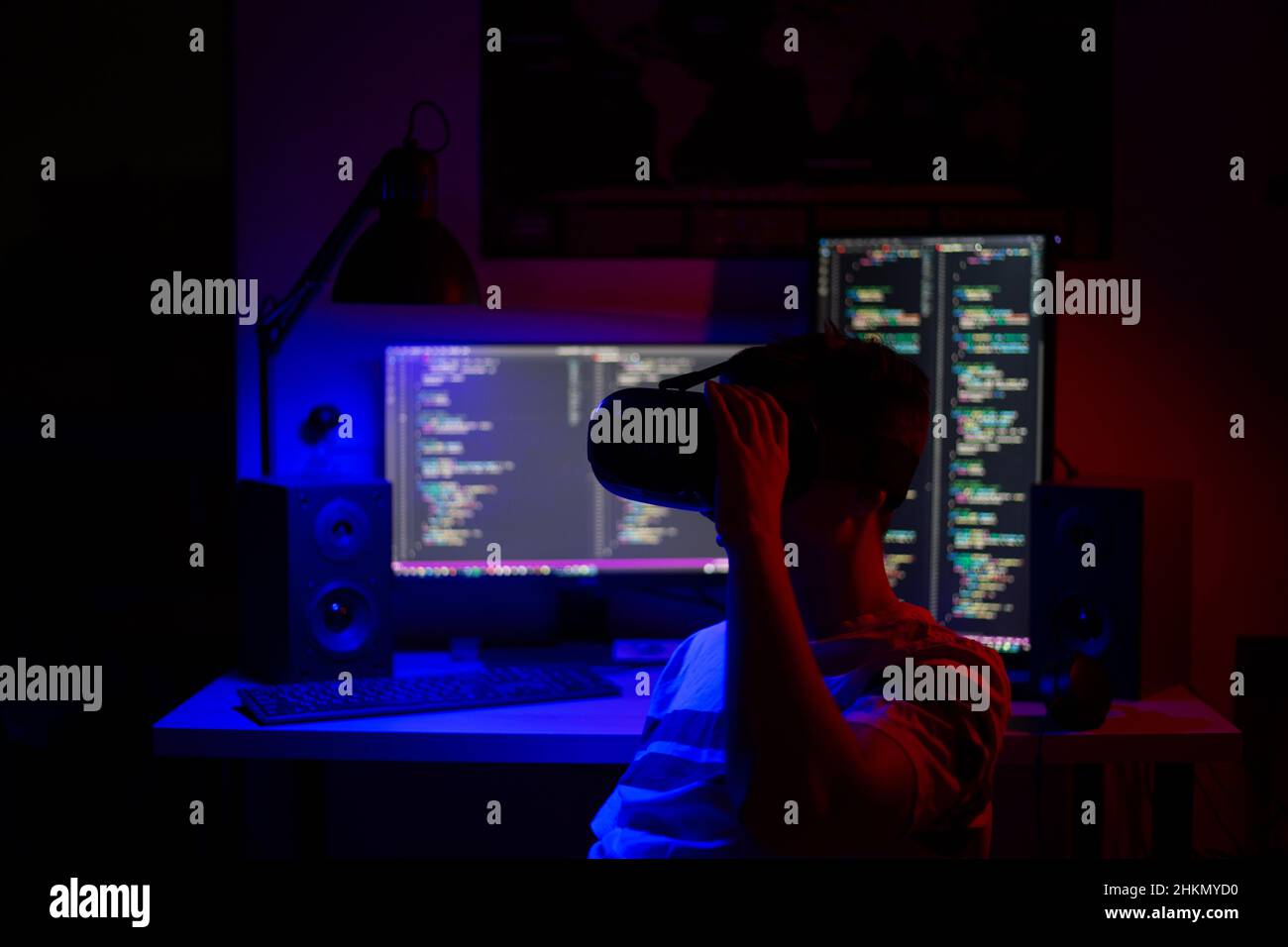 A man in VR glasses sits at a computer in a room at a table at night with blue lighting and programs Stock Photo