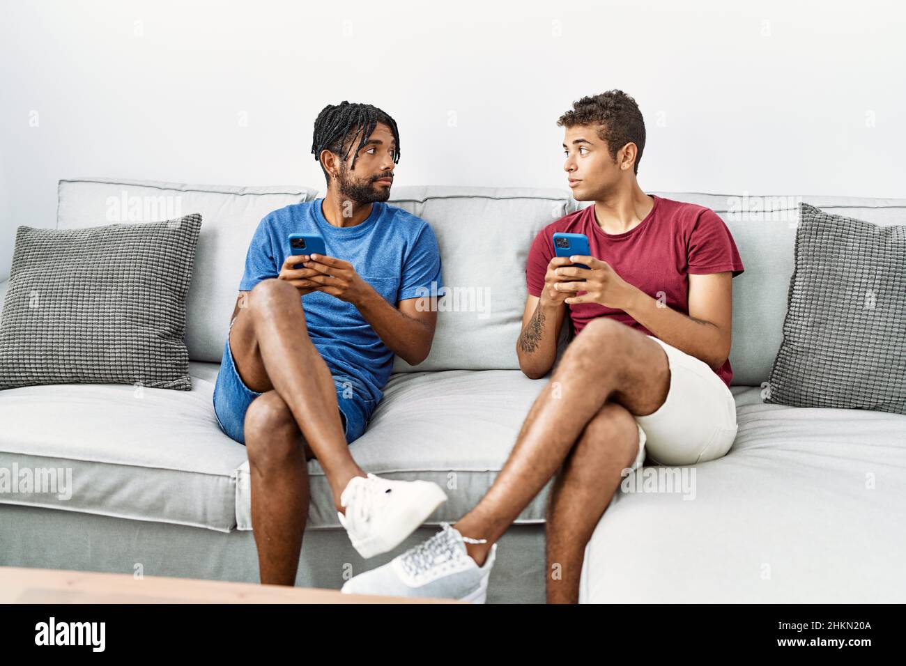 Two men friends using smartphone sitting on sofa at home Stock Photo