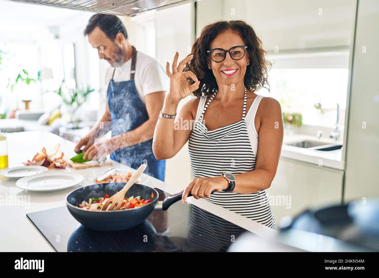 Excellent Cook Middle age couple cooking mediterranean food at home doing ok sign with ...
