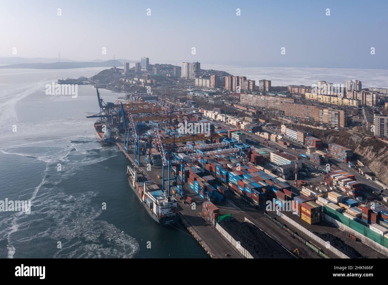 Vladivostok, Russia - January 27, 2022:A top view of the seaport container terminal and city. Winter, a container ship is loading at the berth. Stock Photo