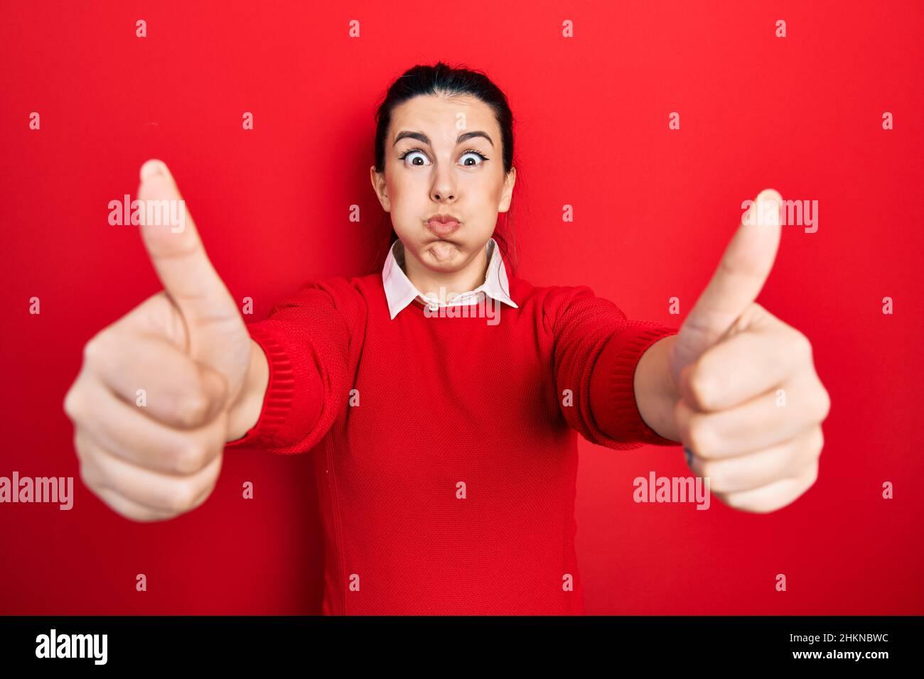 Young hispanic woman doing thumbs up positive gesture puffing cheeks with funny face. mouth inflated with air, catching air. Stock Photo