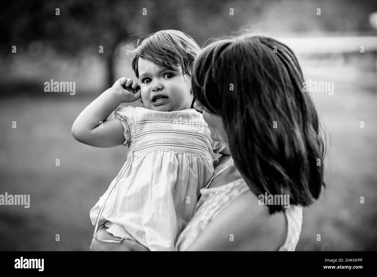 Black and white photo of a mom holding her girl in her arms, girl is crying. Stock Photo
